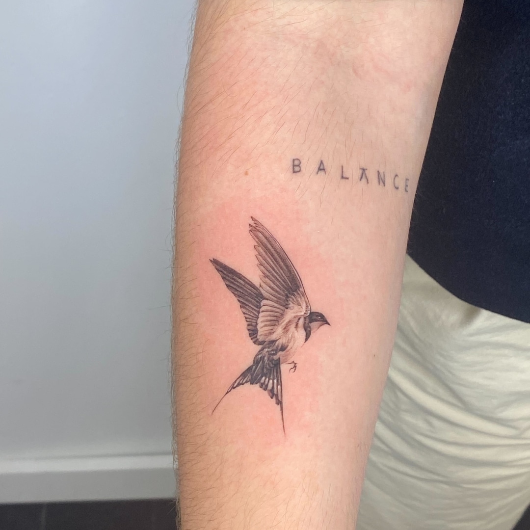 Tattoo of a flying bird with the word 'BALANCE' on the arm