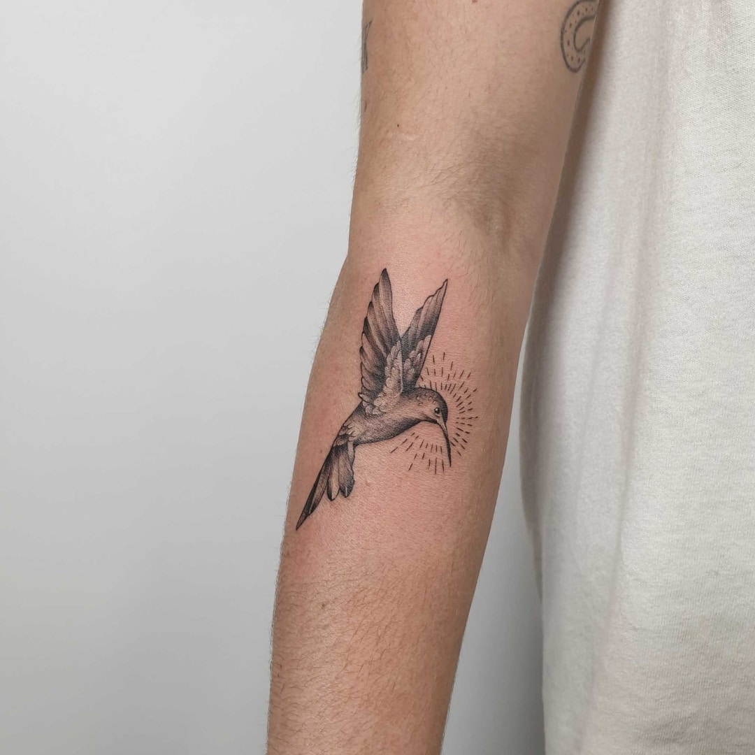 A detailed black and grey tattoo of a bird on a forearm.