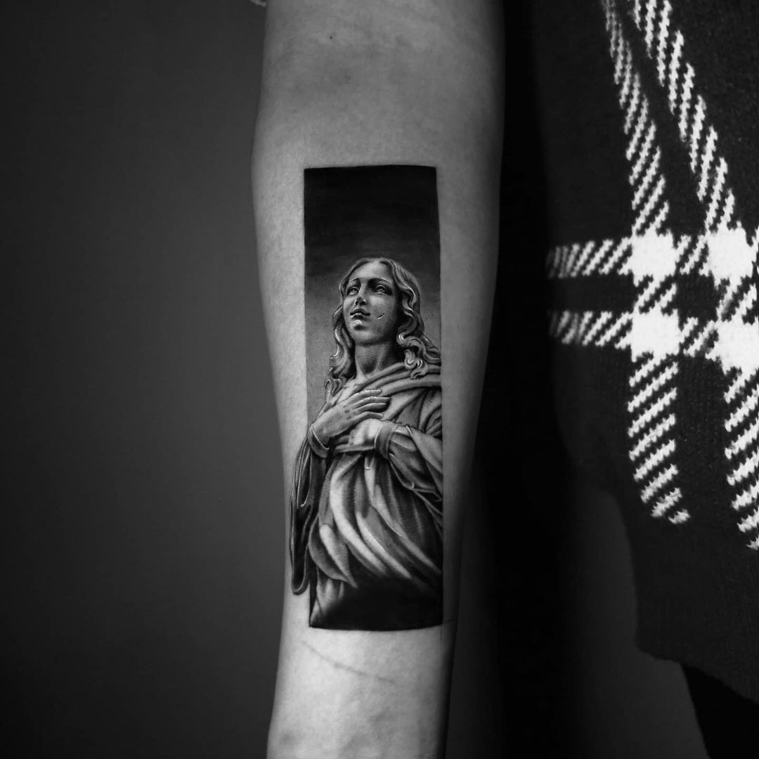 Black and white tattoo of a solemn figure with delicate features and a draped garment.