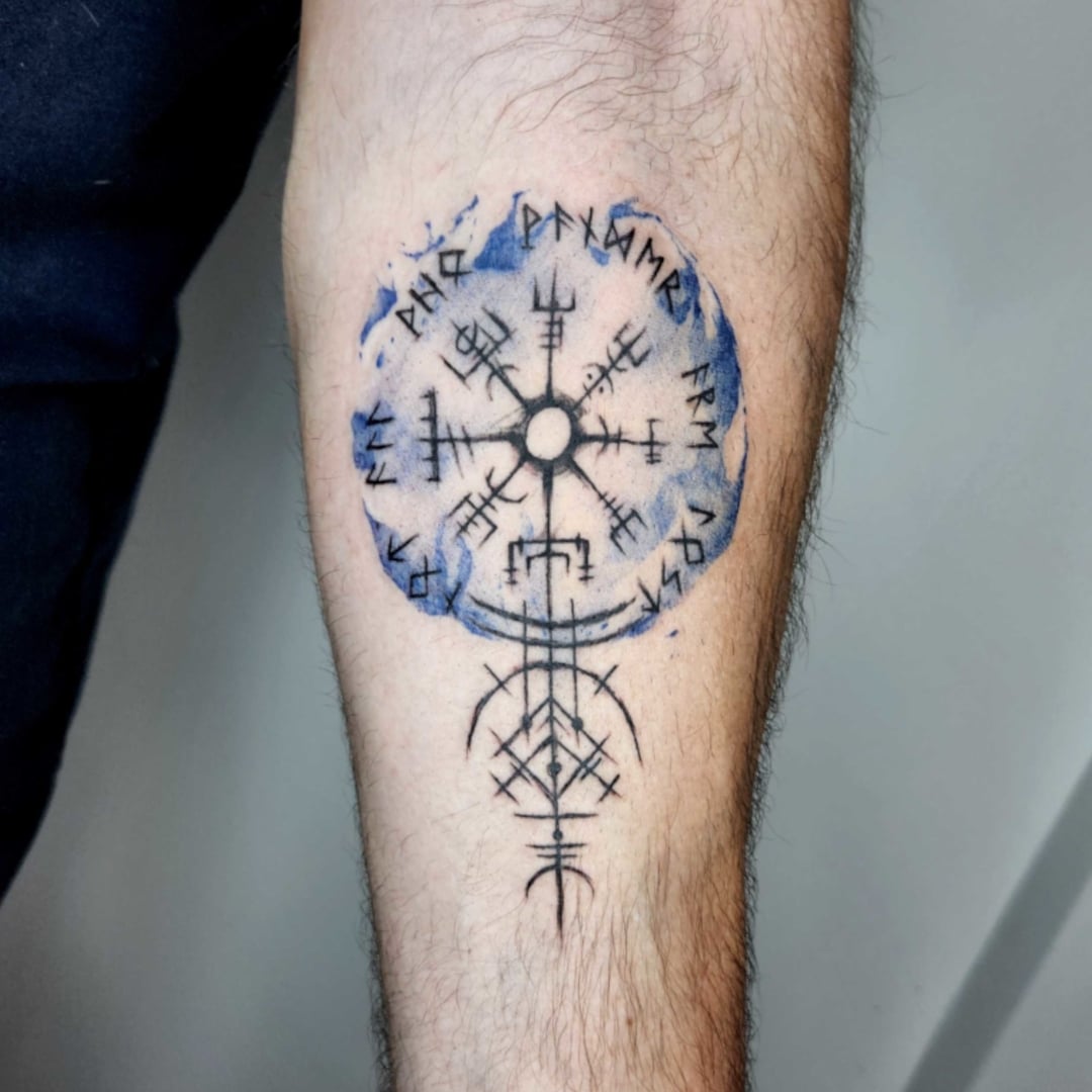Tattoo featuring a symbol with runes and blue watercolor effect