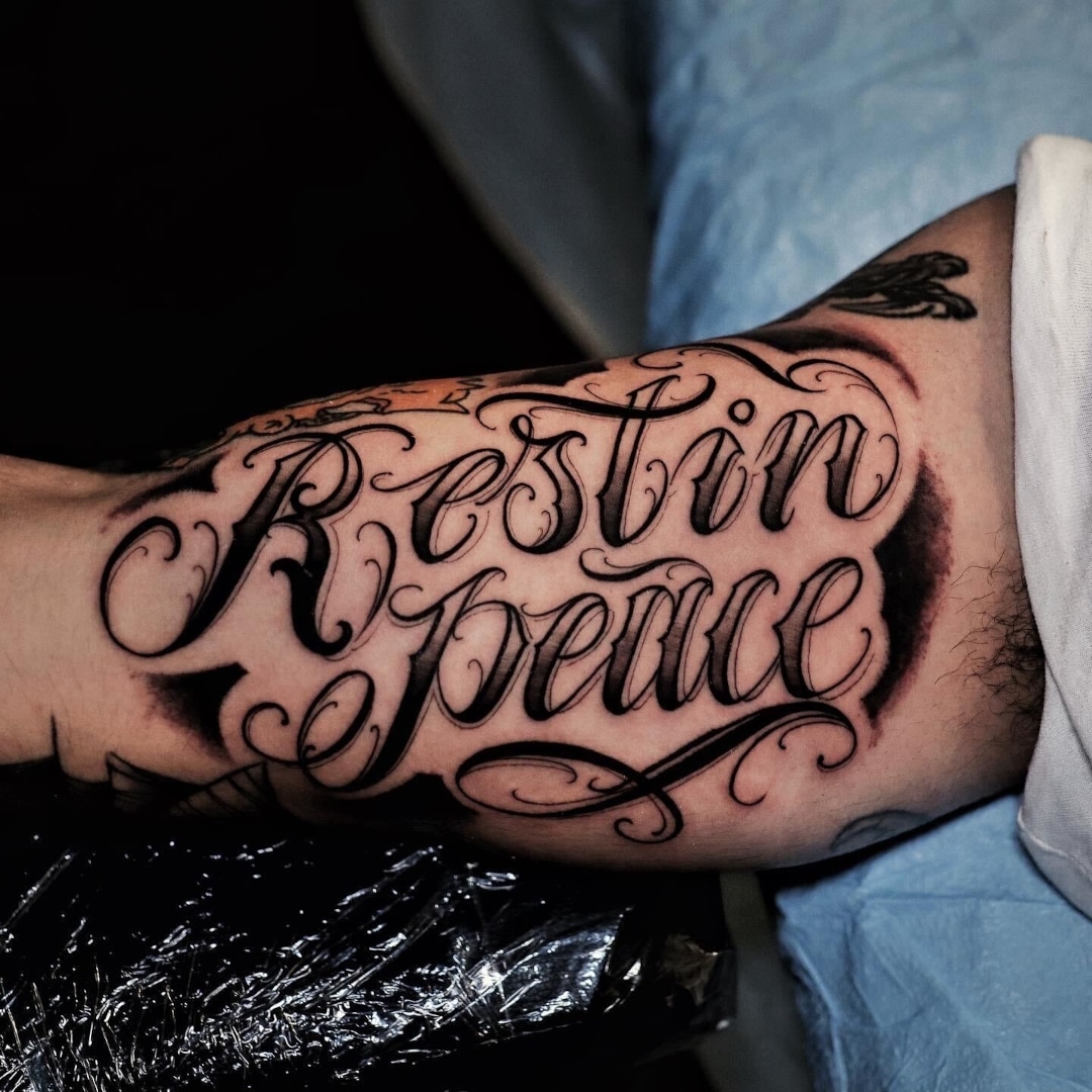 Tattoo on forearm featuring decorative text: Rest in Peace