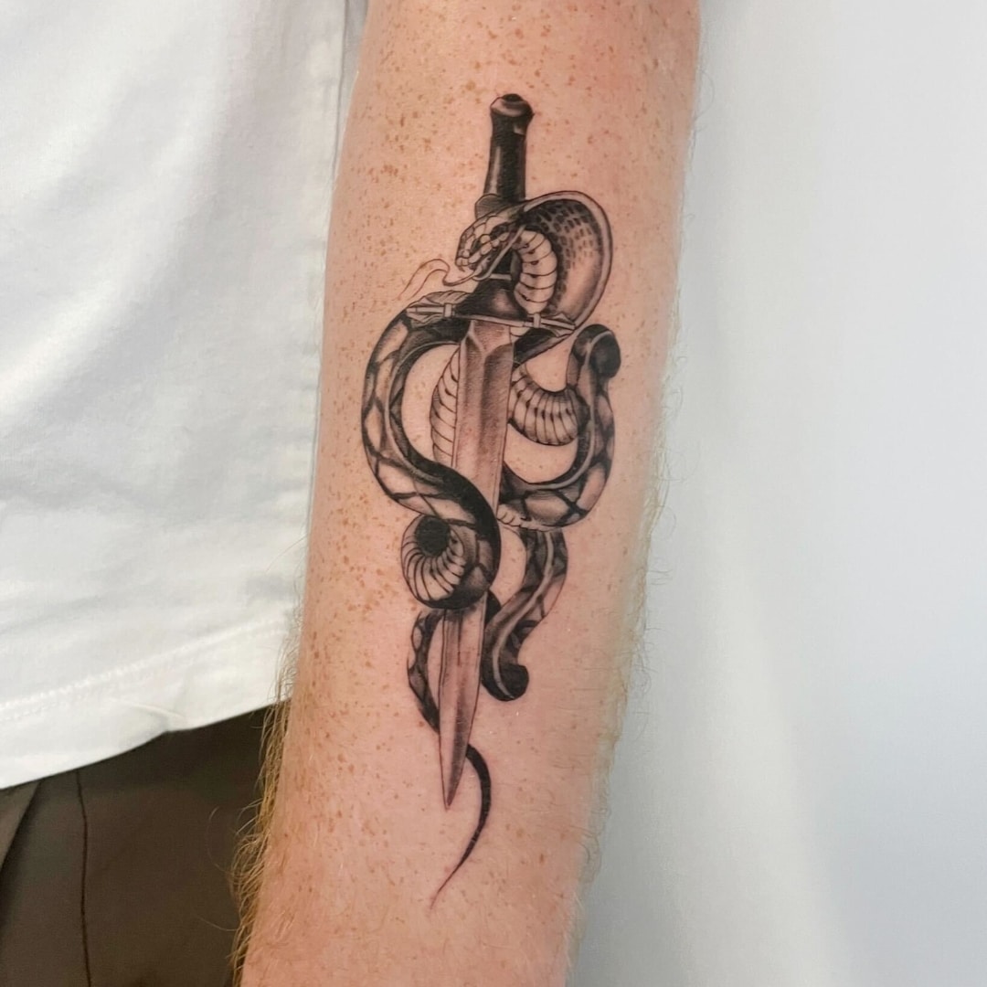 Detailed tattoo of a snake entwined around a dagger on an arm.