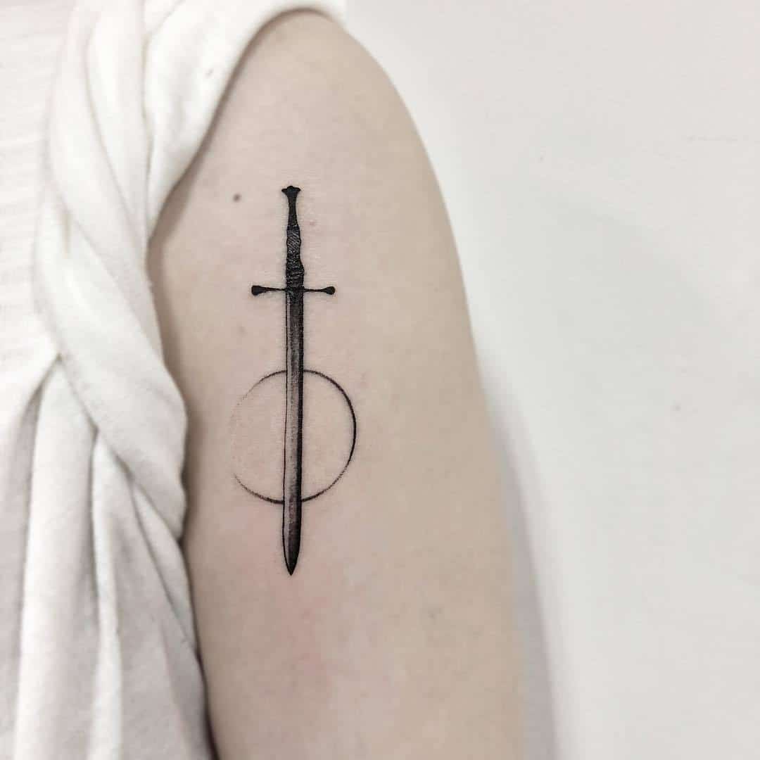 A detailed tattoo of a sword surrounded by a circle on a person's arm.