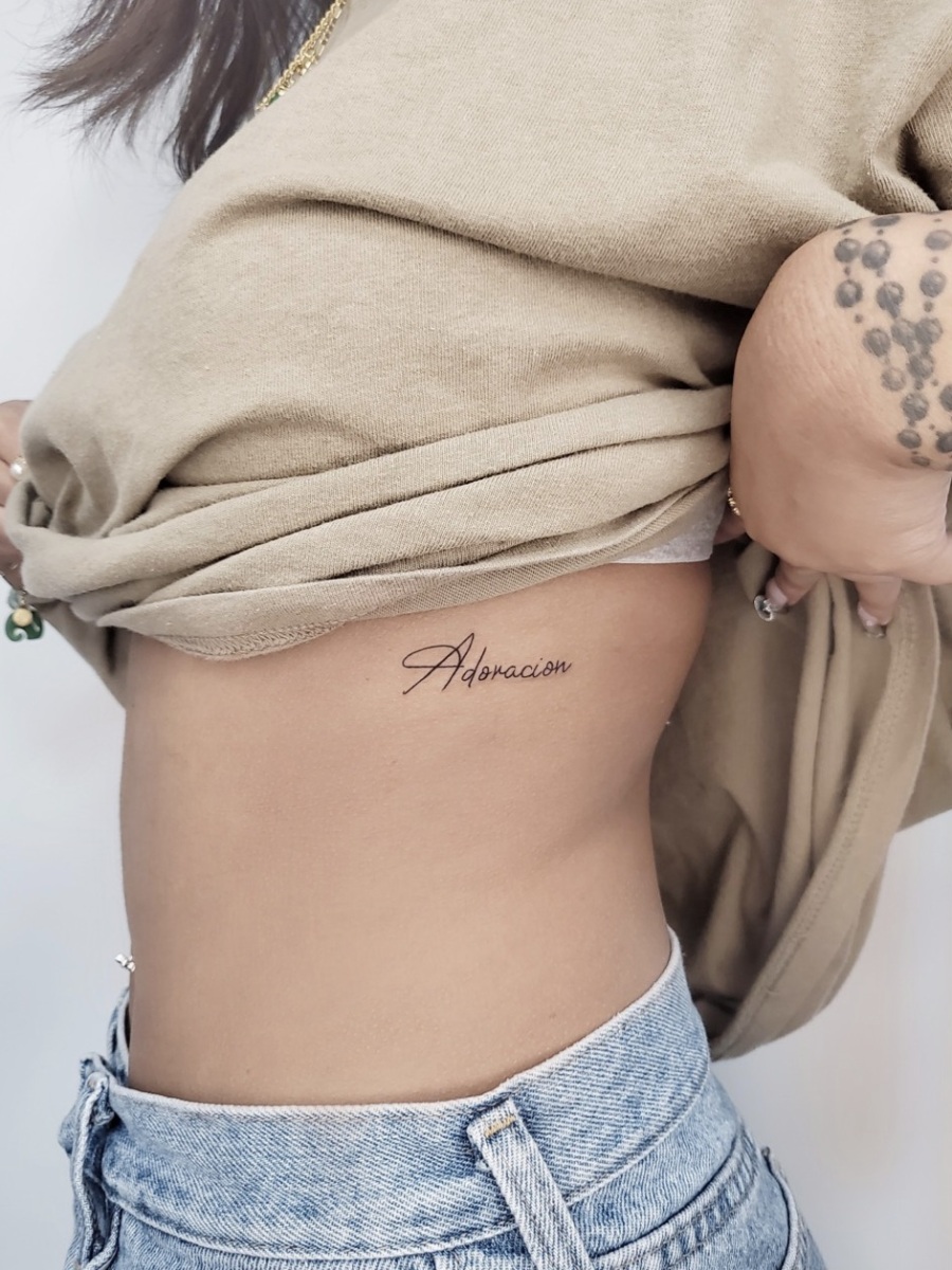 Woman revealing tattoo that says 'Adoracion' on her side