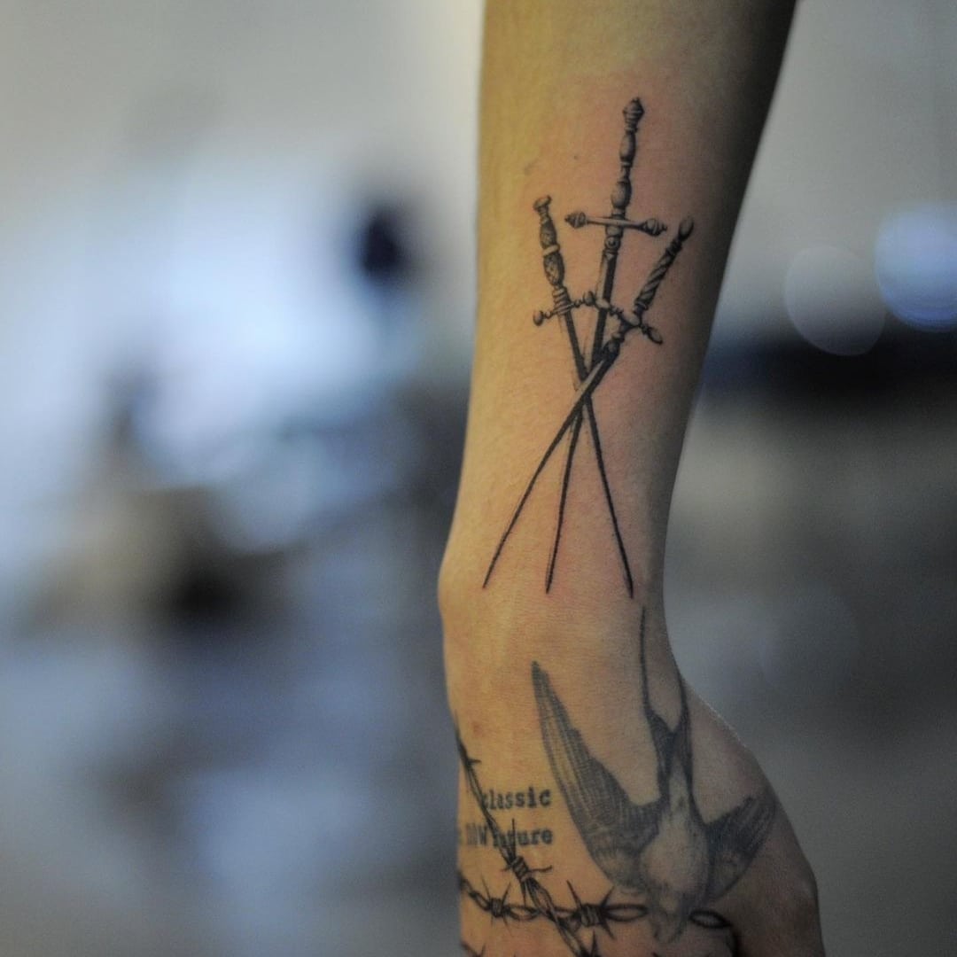 Tattoo of three crossed swords on a forearm